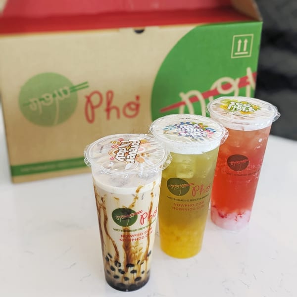 Three Now Phở drinks, including bubble tea, in front of a branded takeout box.