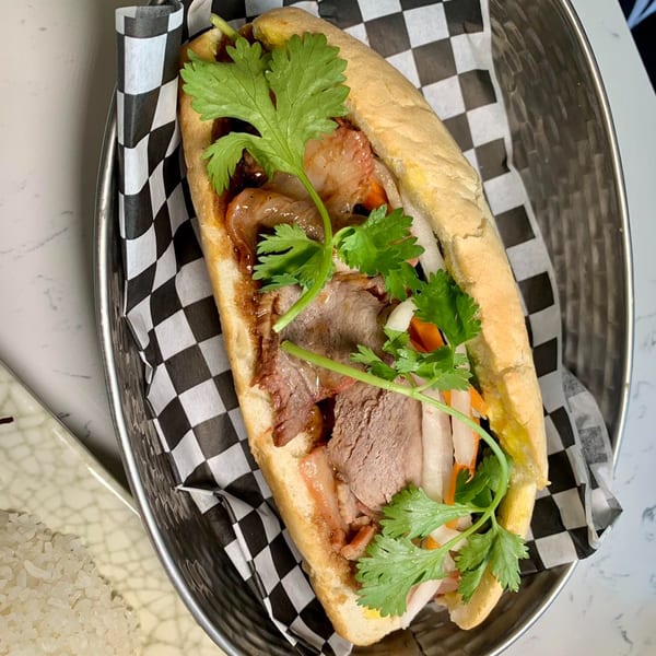 A Vietnamese Banh Mi sandwich with meat, vegetables, and cilantro in a metal basket.