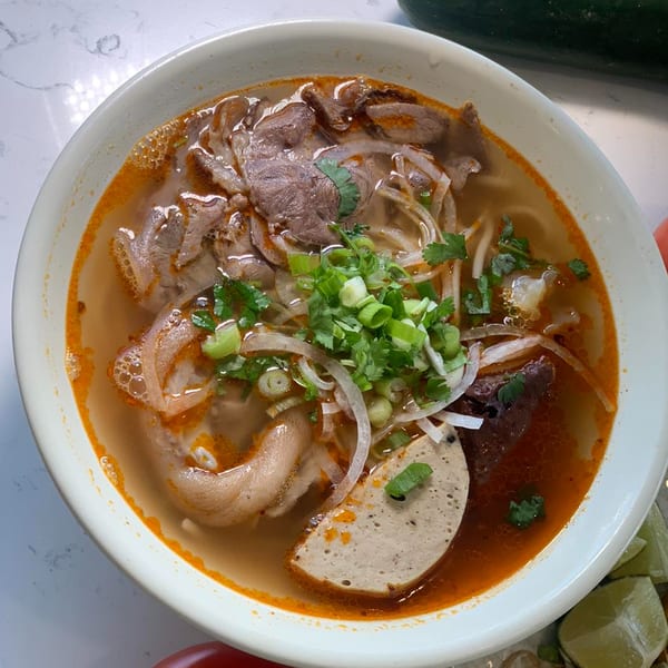 A close-up of a bowl of Now Phở's Vietnamese noodle soup with beef, pork, and herbs.