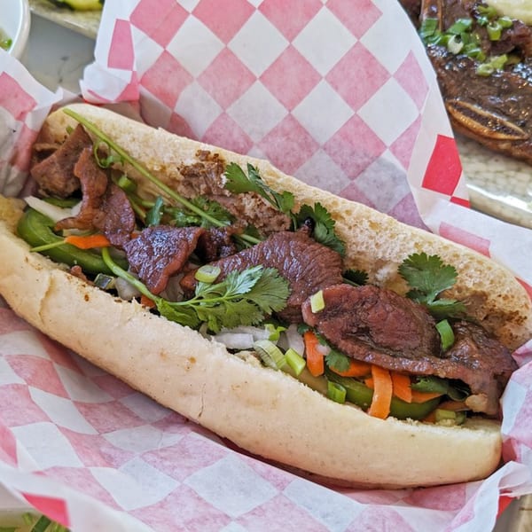 Now Phở's Vietnamese Banh Mi sandwich with grilled beef, cilantro, and pickled vegetables in red checkered paper.